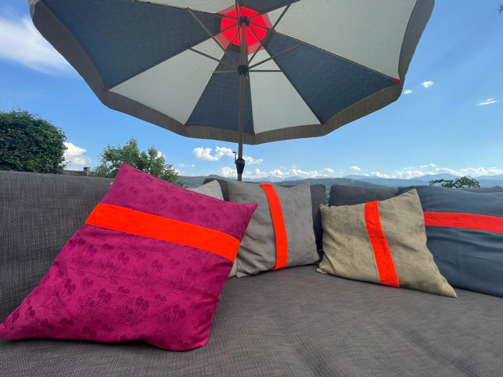 Design-Sonnenschirm von am punkt aus Österreich mit neon-orangem Windventil und farbigen Outdoor-Kissen